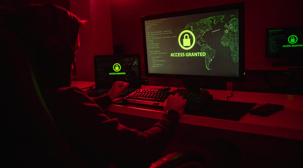 Side view of unrecognizable male in hoodie gaining access to encrypted data through modern computer in dark room