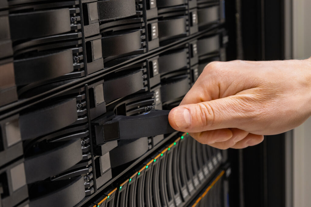 Cropped hand of male IT engineer replacing server drive from rack in SAN at datacenter