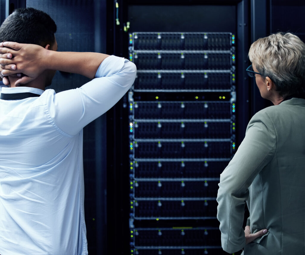Rearview shot of two technicians looking stressed while working in a data centre.